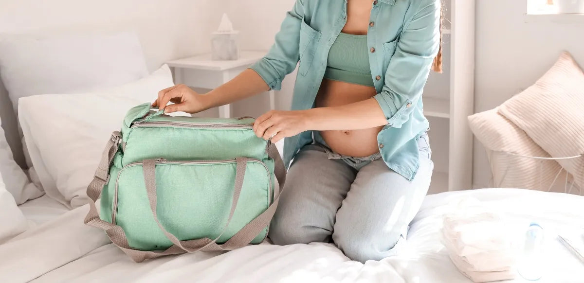 Mulher grávida organizando a bolsa de maternidade com fraldas, roupinhas e produtos de higiene.