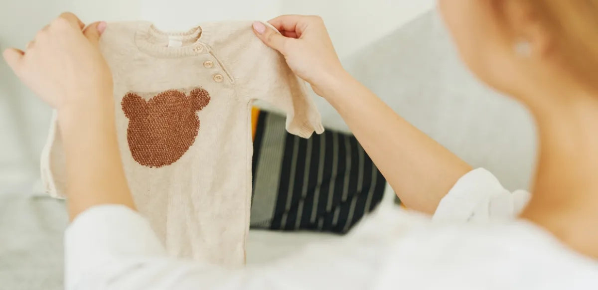 Pessoa segurando um body de bebê em tricot bege com estampa de ursinho, ideal para os dias mais frios.