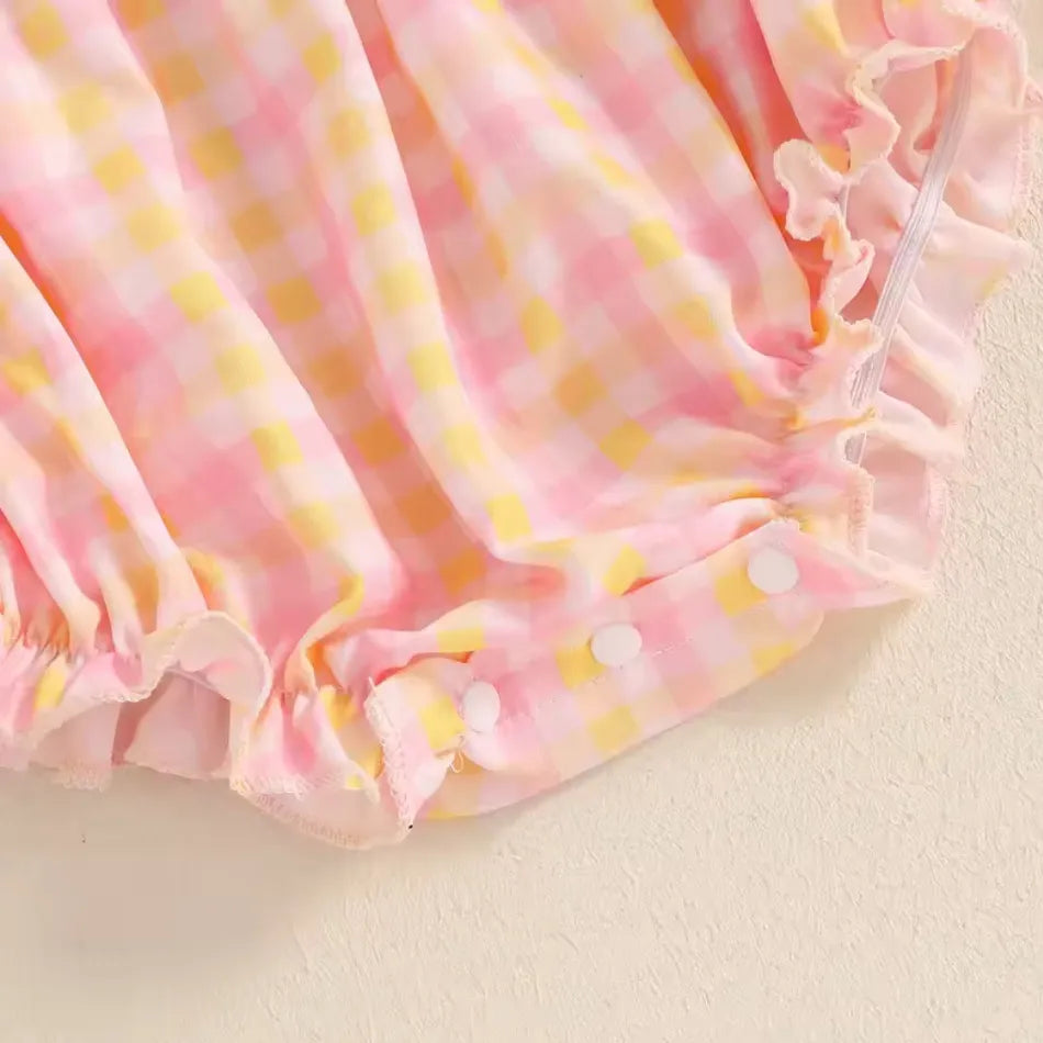 Detalhe do fechamento inferior do body bebê, com botões de pressão para facilitar a troca de fraldas. Tecido xadrez rosa e amarelo com babadinhos delicados na barra.