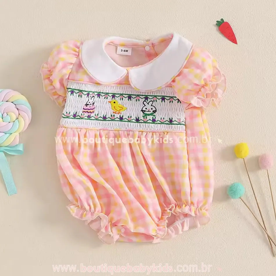 Body bebê temático de Páscoa em exibição, decorado com bordado delicado, gola clássica branca e babadinhos charmosos nas mangas e barra.