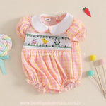 Body bebê temático de Páscoa em exibição, decorado com bordado delicado, gola clássica branca e babadinhos charmosos nas mangas e barra.