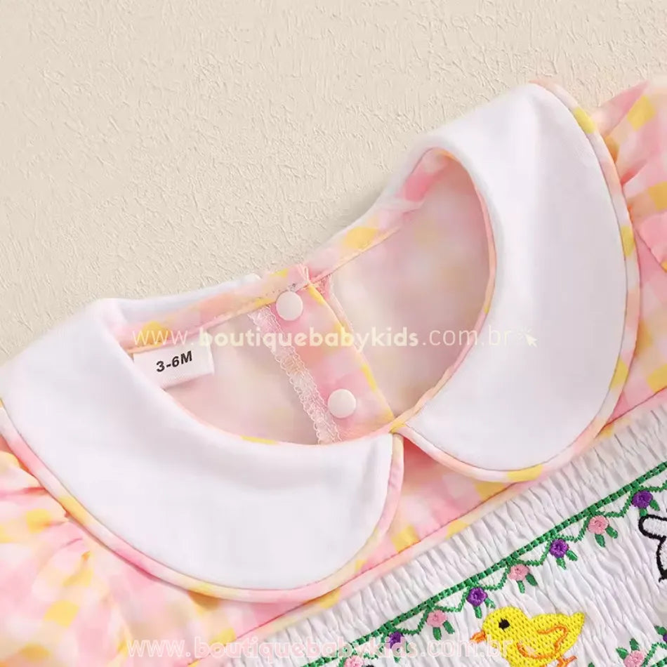 Gola arredondada branca com detalhe em viés amarelo, fechamento por botões de pressão na parte traseira, trazendo praticidade e um toque clássico ao look.