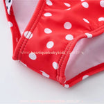 Detalhe da costura e acabamento da parte inferior do maiô infantil engana mamãe Joaninha, com estampa de bolinhas brancas sobre fundo vermelho.