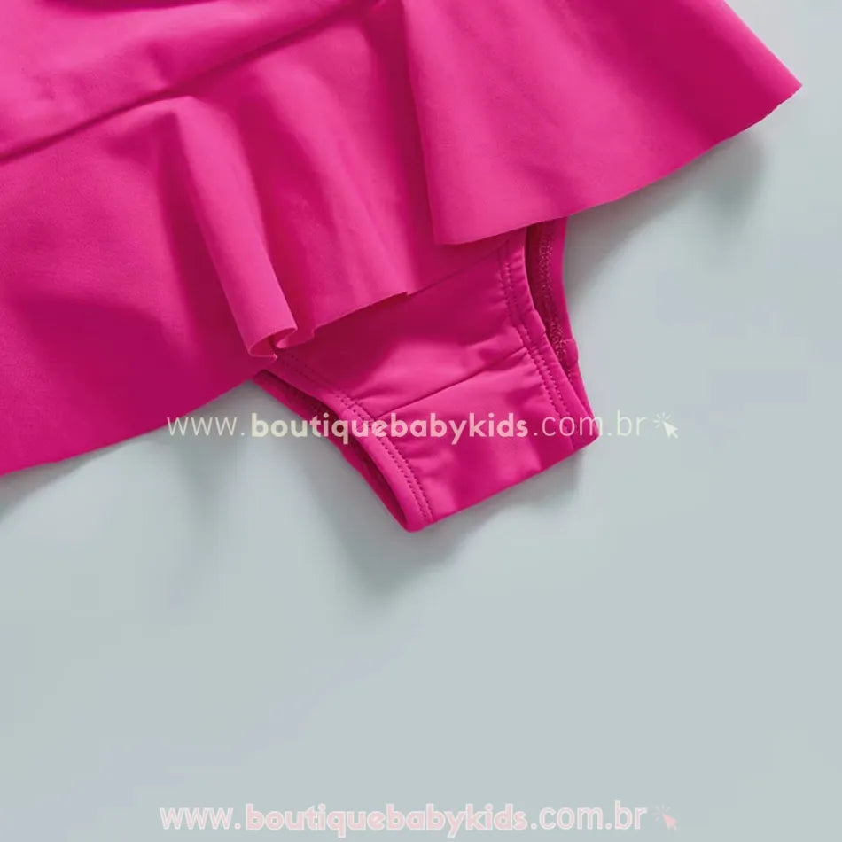 Detalhe da parte inferior do maiô infantil rosa, destacando a saia delicada acoplada e o acabamento do tecido.