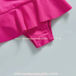 Detalhe da parte inferior do maiô infantil rosa, destacando a saia delicada acoplada e o acabamento do tecido.