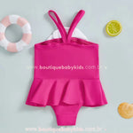 Vista traseira do maiô rosa, mostrando a saia fluida e as alças duplas cruzadas para um toque delicado.