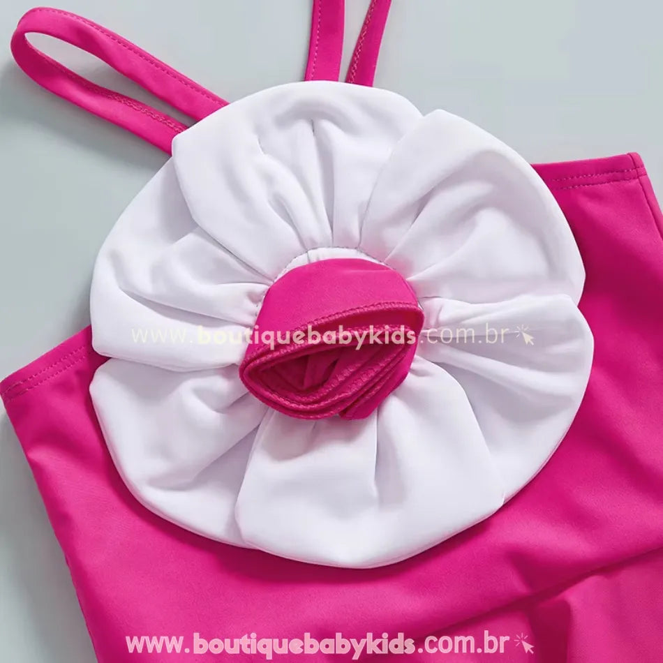 Close da grande flor branca com centro rosa costurada na frente do maiô, criando um efeito tridimensional encantador.