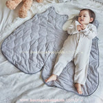 Saco de dormir cinza aberto, mostrando seu interior acolchoado e macio, com bebê deitado ao lado para comparação de tamanho.