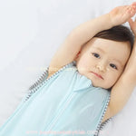 Bebê deitado e sorrindo, com os braços levantados acima da cabeça, vestindo o saco de dormir azul claro com bordado discreto de smile.