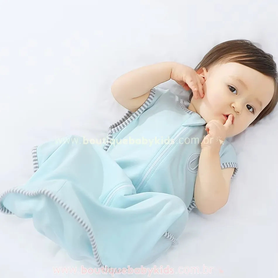 Bebê deitado, com uma expressão tranquila, usando o saco de dormir azul claro, com destaque para o bordado delicado e o fechamento frontal.