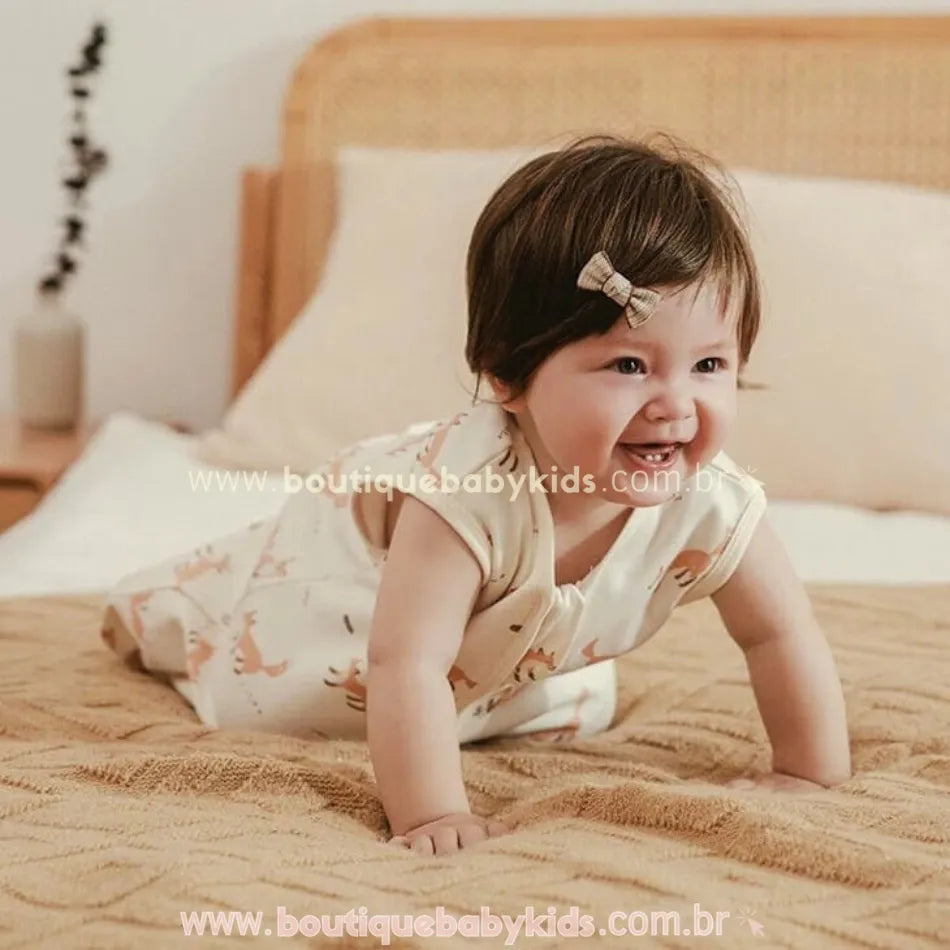 Bebê sorridente engatinhando sobre a cama enquanto veste o saco de dormir sem mangas, com estampa de raposas em tom caramelo sobre fundo creme.