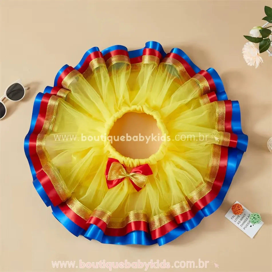 Saia infantil Branca de Neve aberta em formato circular, com tule volumoso amarelo e detalhes de fita de cetim azul e vermelho, além de laço decorativo.