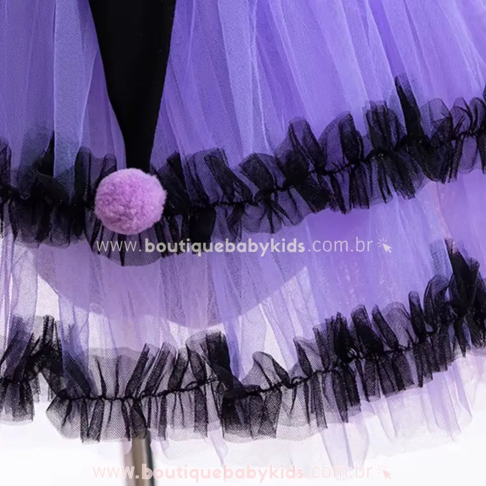  Saia rodada do vestido infantil de bruxinha, feita de camadas de tule roxo, com babados pretos e pompons decorativos.