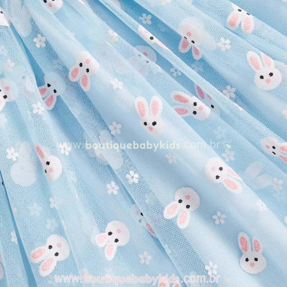 Close na saia do vestido azul, revelando a leveza do tule e a charmosa estampa de coelhinhos brancos com detalhes florais, proporcionando um visual encantador e delicado. 