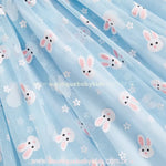 Close na saia do vestido azul, revelando a leveza do tule e a charmosa estampa de coelhinhos brancos com detalhes florais, proporcionando um visual encantador e delicado. 