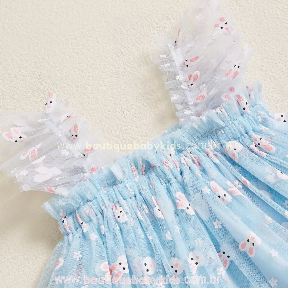 Parte superior do vestido azul, com alças de tule franzido e elástico na cintura, garantindo um ajuste confortável. A estampa de coelhinhos brancos e flores destaca-se sobre o fundo azul suave. 