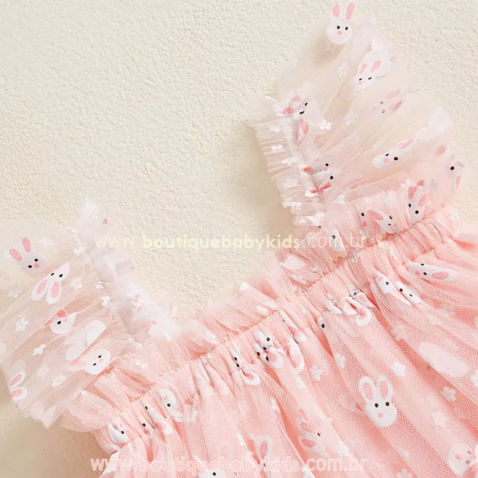 Detalhe do ombro do vestido rosa, com alças de tule franzido estampadas com coelhinhos brancos e pequenas flores brancas, trazendo um toque delicado e encantador à peça. 