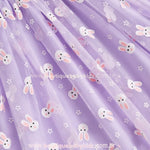 Close na saia do vestido lilás, mostrando a leveza do tecido e os detalhes da estampa de coelhinhos brancos e flores, conferindo um toque lúdico à peça. 