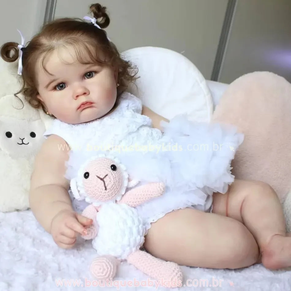 Boneca Bebê Reborn Camila deitada, segurando um bichinho de crochê, com expressão serena e aparência hiper-realista.
