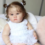 Boneca Bebê Reborn Camila sentada na poltrona, usando vestido branco com babados, em pose realista e delicada.