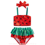 Conjunto Biquíni Bebê Melancia Summer completo em fundo branco. O kit inclui top vermelho com sementes pretas, calcinha com babado verde listrado imitando a casca e uma faixa de cabelo vermelha com laço.