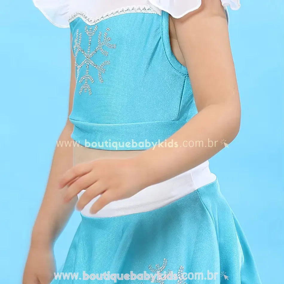Close do top azul brilhante do biquíni infantil temático da Elsa, com mangas curtas transparentes e detalhe de floco de neve bordado em strass.