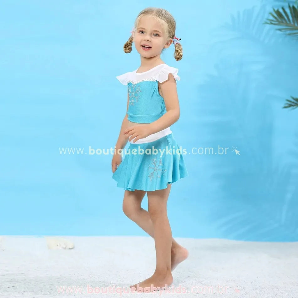 Menina vestindo o biquíni infantil Frozen Princesa Elsa em um ambiente de praia, destacando a saia rodada azul clara e o top com mangas delicadas.