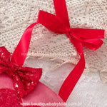 Laço de fita vermelha para amarração nos ombros, permitindo ajuste perfeito e um acabamento delicado. Fundo com renda branca e decoração temática romântica.