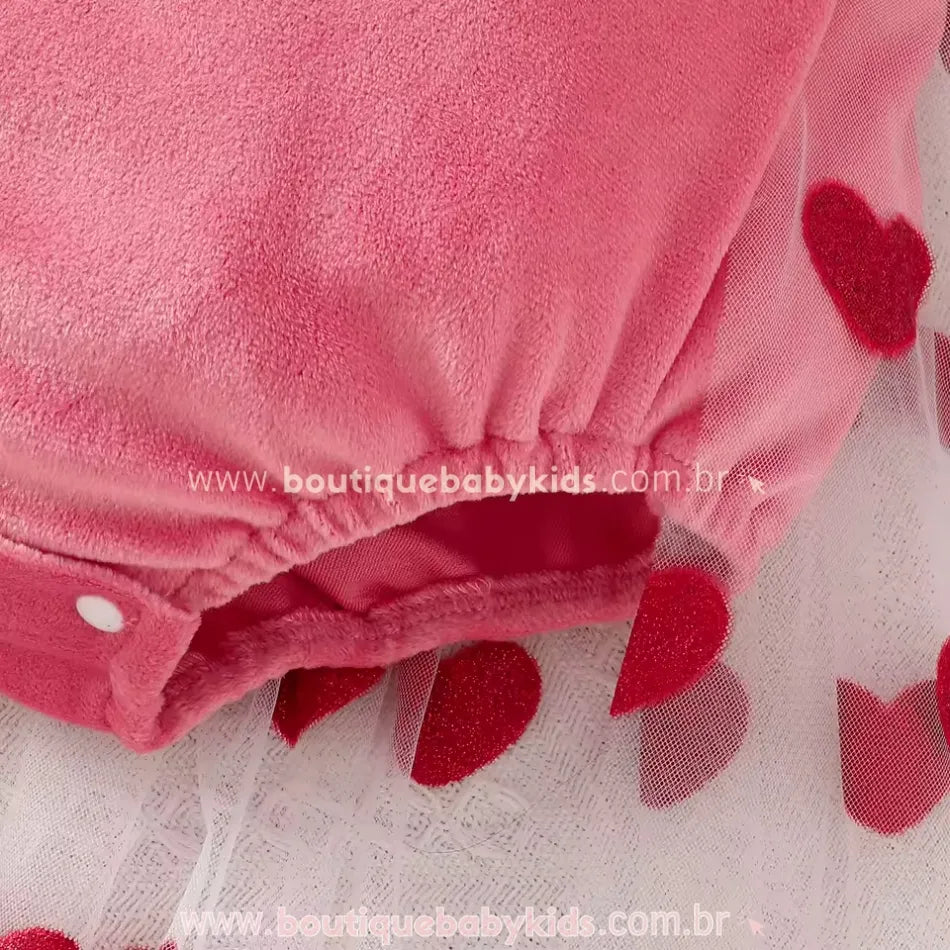 Detalhe da parte inferior do body em tecido aveludado rosa, com elástico confortável nas perninhas e fechamento por botões de pressão. O tule com corações vermelhos dá um toque delicado e encantador.