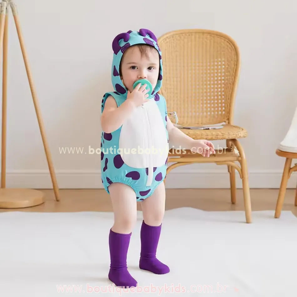 Bebê vestindo o body fantasia Monstrinho Sulley, com capuz e meias roxas combinando, em um ambiente aconchegante.