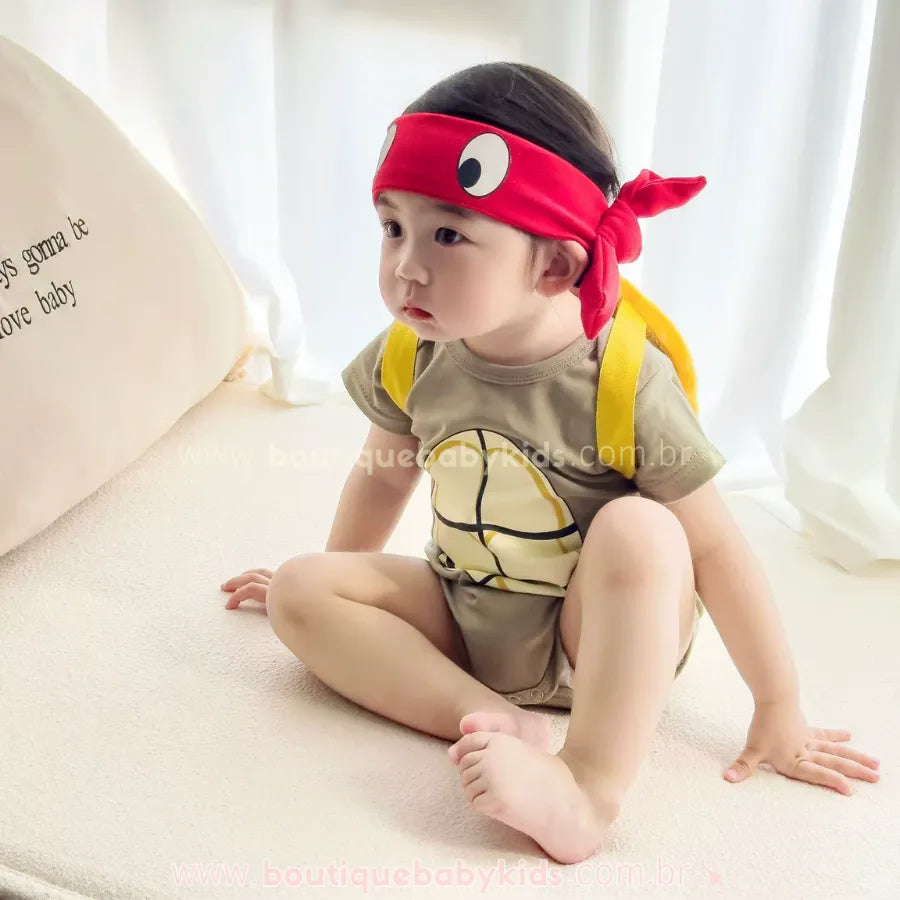 Bebê sentado vestindo Body Fantasia Tartaruga Ninja com faixa vermelha na cabeça, ideal para fotos de mesversário neste tema.