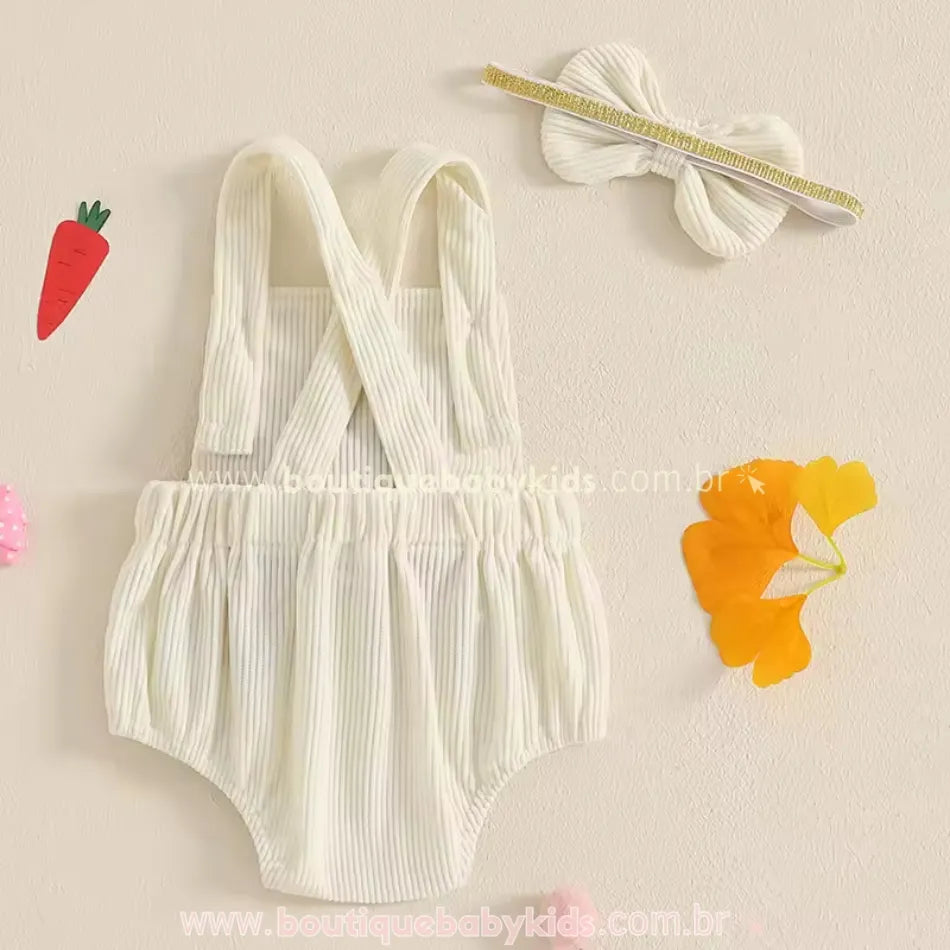 Vista traseira do body bebê jardineira na cor creme, destacando as alças cruzadas ajustáveis e a faixa de cabelo combinando, com detalhe em elástico dourado. 