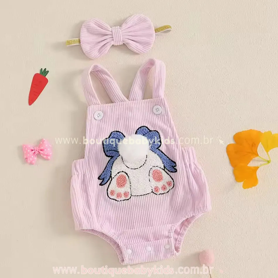 Body bebê jardineira cor-de-rosa com estampa de coelhinha, bordado detalhado com laço azul e rabinho de pompom. Acompanha faixa de cabelo combinando. 