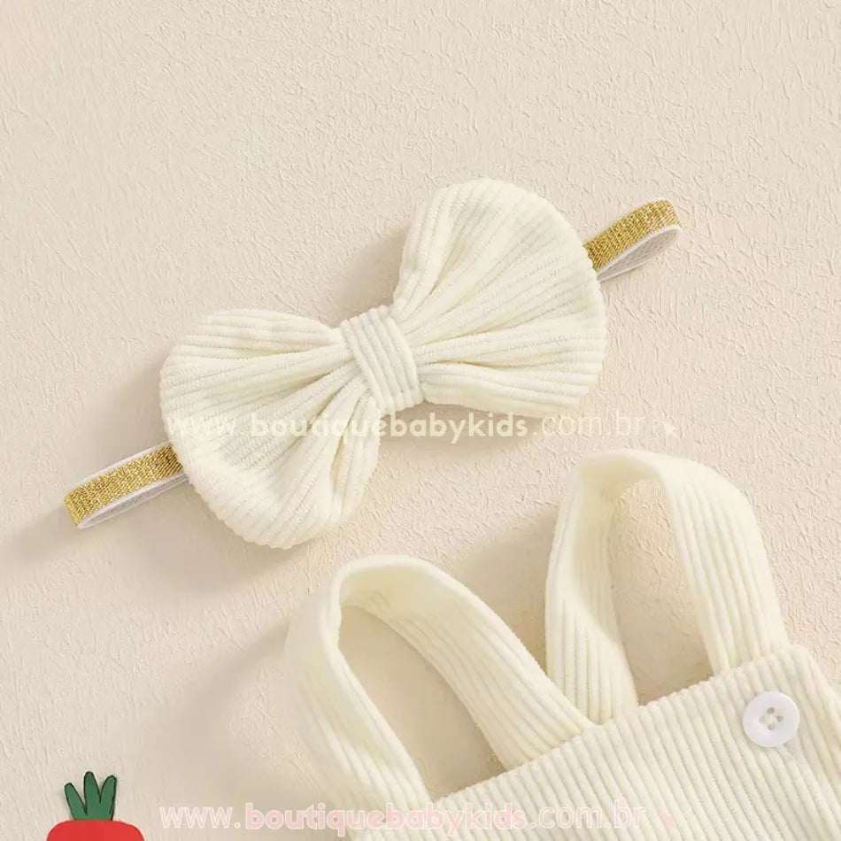 Faixa de cabelo creme com laço estruturado e elástico dourado combinando com a jardineira. 