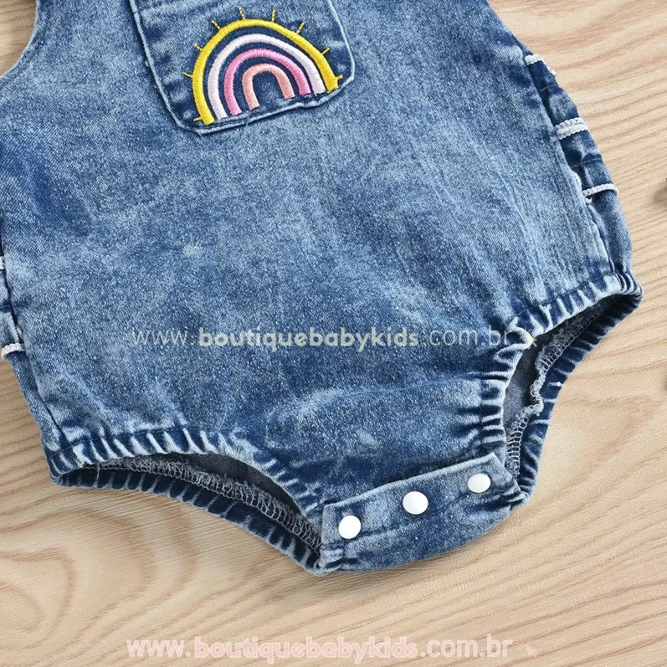 Bordado de arco-íris em cores vibrantes no bolso frontal do body jardineira, proporcionando um toque lúdico à peça.