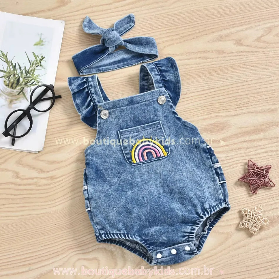 Conjunto de body jardineira jeans com faixa de cabelo em um fundo de madeira, destacando os detalhes delicados da peça.