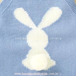 Estampa de coelhinho branco na parte traseira do body bebê jardineira azul, com um rabinho de pompom macio em destaque. 