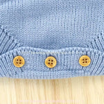 Vista detalhada do acabamento em tricot azul na parte inferior do body bebê jardineira, com três botões de madeira para fechamento. 