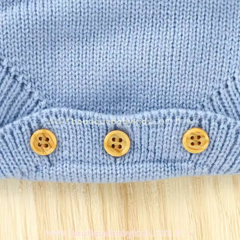 Vista detalhada do acabamento em tricot azul na parte inferior do body bebê jardineira, com três botões de madeira para fechamento. 