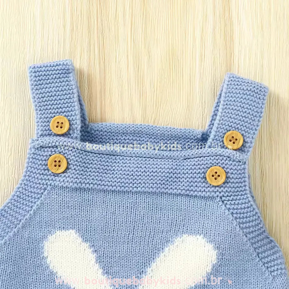 Close nas alças do body bebê jardineira azul, destacando os botões de madeira e o acabamento em tricot. 