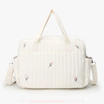 Vista traseira da bolsa maternidade Delicadeza Floral, destacando o design minimalista com bordado floral, alça de ombro ajustável e laterais com presilhas metálicas para encaixe no carrinho do bebê.