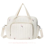 Bolsa maternidade delicada em tom off-white com bordado floral minimalista em rosa e verde. Modelo estruturado com alças duplas e um bolso frontal espaçoso com zíper.