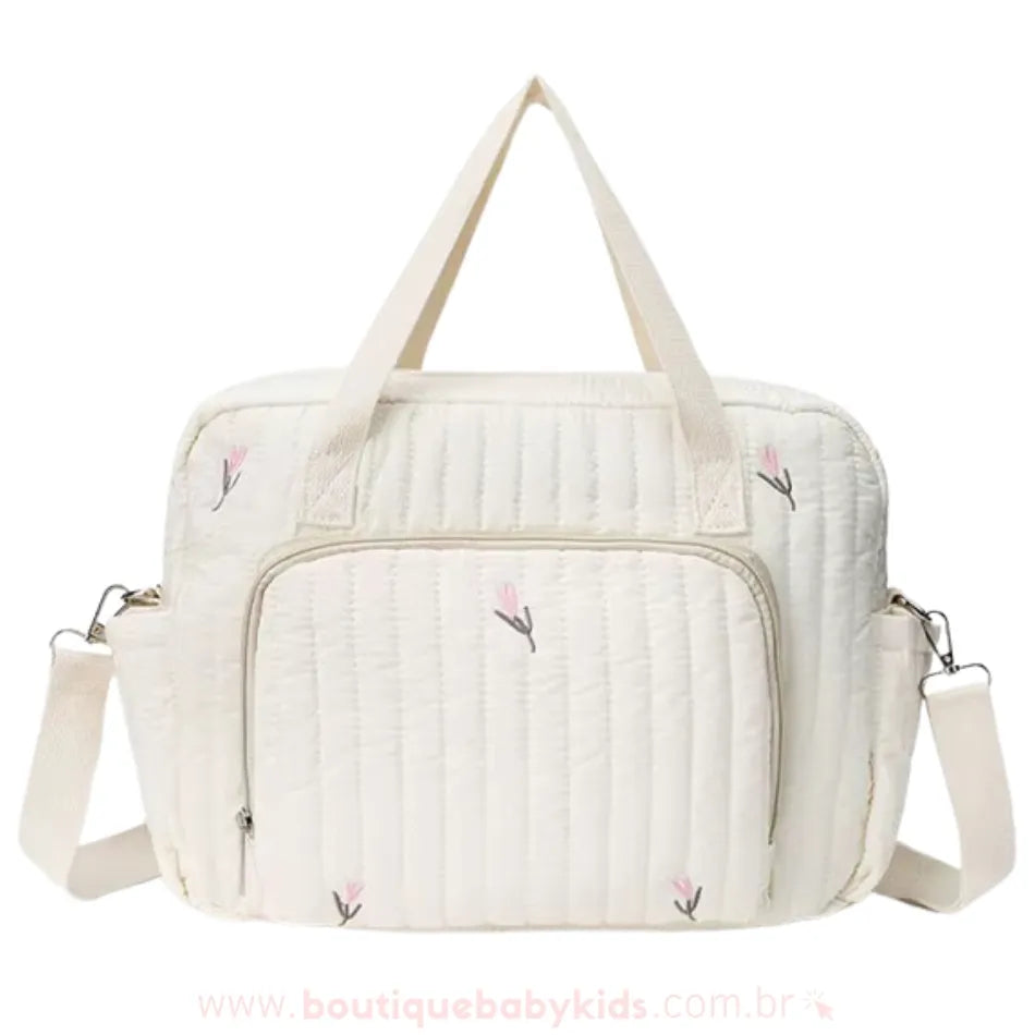 Bolsa maternidade delicada em tom off-white com bordado floral minimalista em rosa e verde. Modelo estruturado com alças duplas e um bolso frontal espaçoso com zíper.