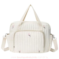 Bolsa maternidade delicada em tom off-white com bordado floral minimalista em rosa e verde. Modelo estruturado com alças duplas e um bolso frontal espaçoso com zíper.