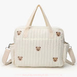 Parte frontal da Bolsa Maternidade Ursinho Aconchego, com bordados de carinhas de ursinho sobre tecido matelassado bege.