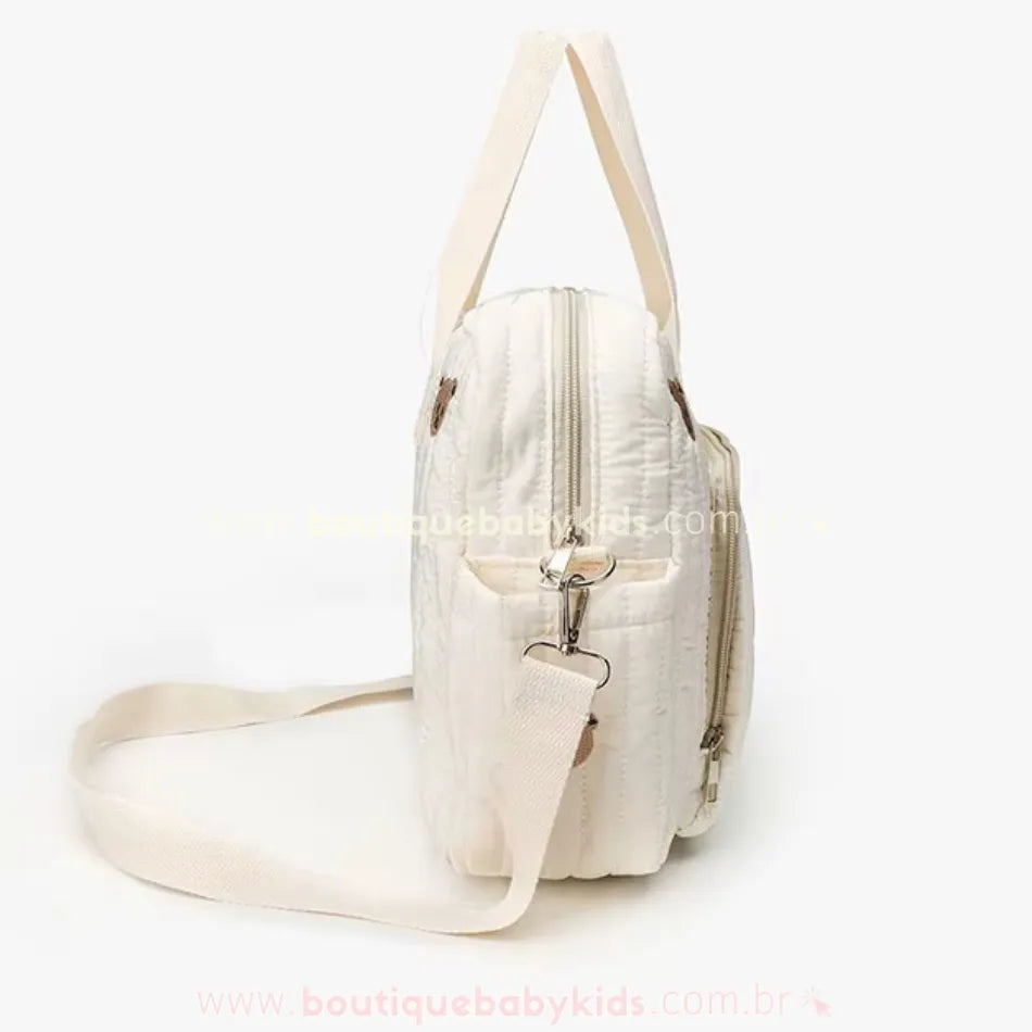 Vista lateral da Bolsa Maternidade Ursinho Aconchego, destacando a alça transversal removível e o tecido acolchoado com detalhes sutis.