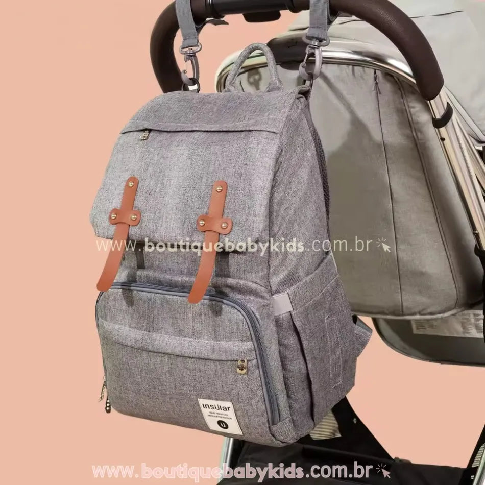Mochila maternidade Insular Travel na cor cinza pendurada em um carrinho de bebê, mostrando sua funcionalidade para passeios e praticidade no dia a dia.