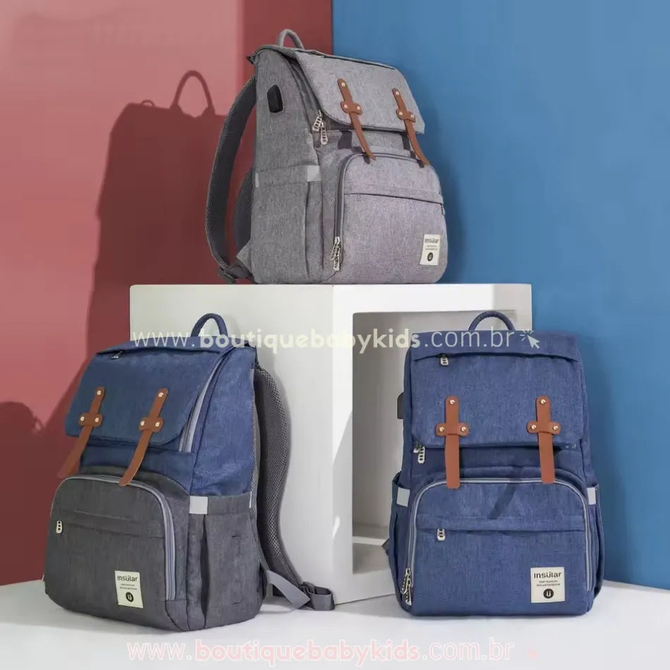 Conjunto de três mochilas maternidade Insular Travel em tons de cinza e azul, expostas em um fundo vermelho e azul, destacando o design moderno e sofisticado.