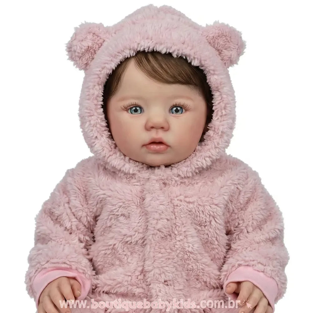 Foto de estúdio com fundo branco mostrando o rosto da Boneca Bebê Reborn Amira de frente. Ela está com o capuz de ursinho rosa levantado, destacando seus olhos claros e expressão angelical.