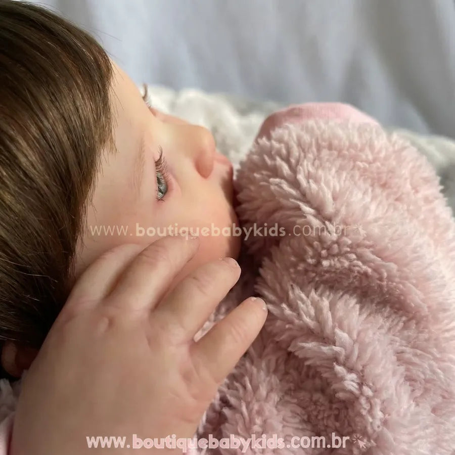 Close detalhado do perfil do rosto da Boneca Reborn Amira, mostrando a textura realista da pele, os cílios delicados e o cabelo castanho. A mão da boneca toca suavemente a bochecha.